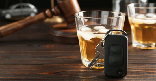 Car keys next to alcoholic drink in the foreground with a judge's gavel in the background