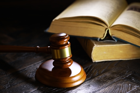 A wooden gavel resting on a dark wooden surface, placed beside two open law books, symbolizing justice and legal proceedings.